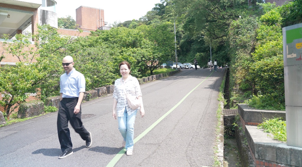 Long and Vi walking side by side down a tree-lined road on a bright day.
