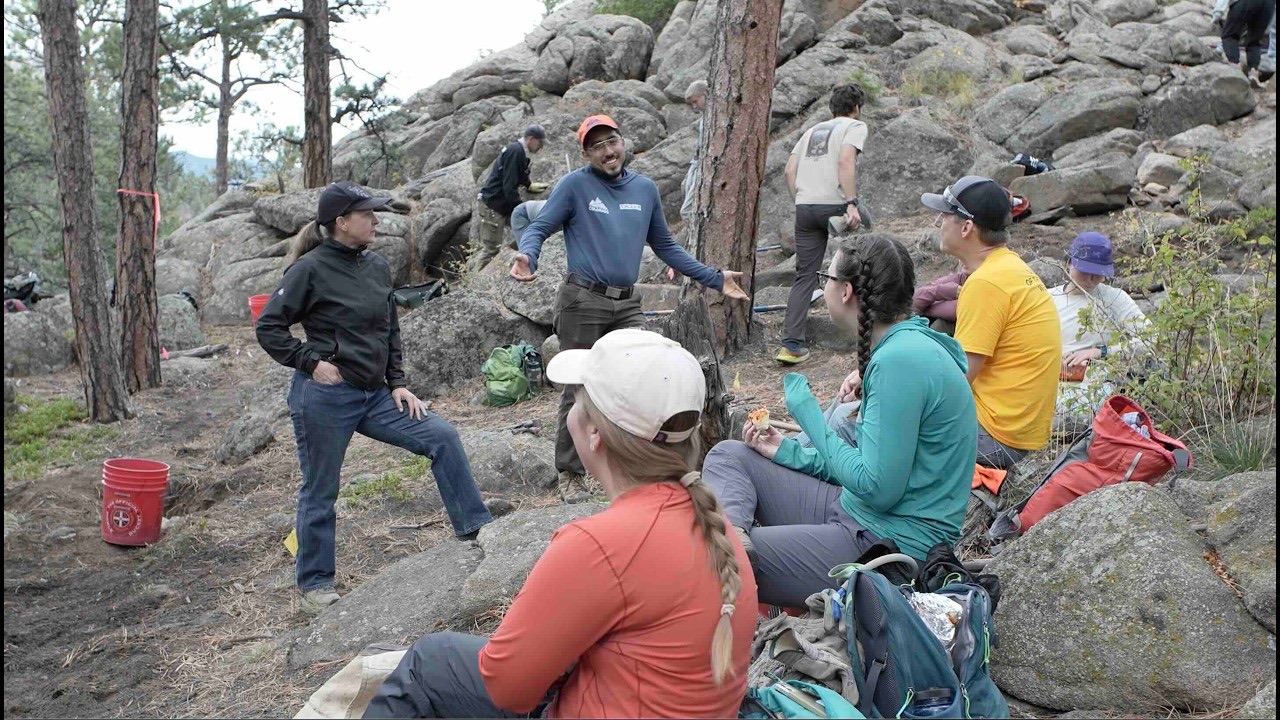 Một nhóm tình nguyện viên quây quần giữa rừng thông và những tảng đá trong ngày dự án của Volunteers for Outdoor Colorado.